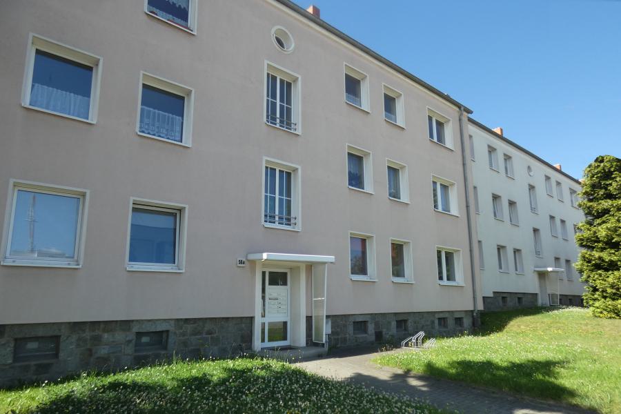 Dreistöckiges Mehrfamilienhaus mit Grünfläche davor.