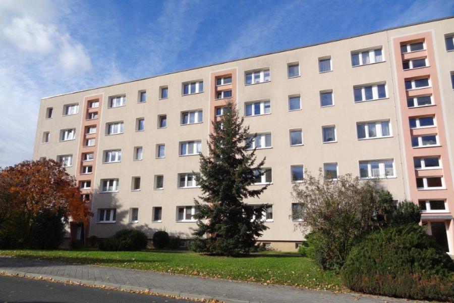 Mehrstöckiges Wohngebäude mit Grünfläche, Weg, Straße und Bäumen davor.