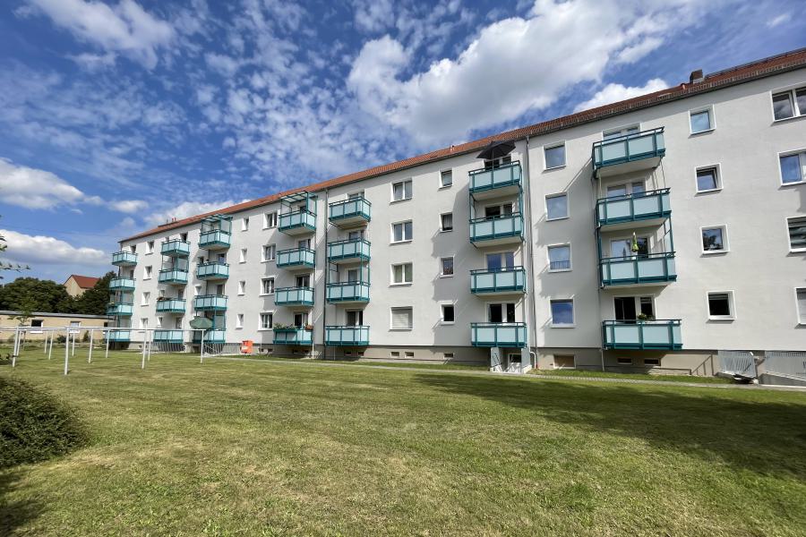 Mehrstöckiges Wohngebäude mit Balkonen, Grünfläche und Wäscheplatz davor.